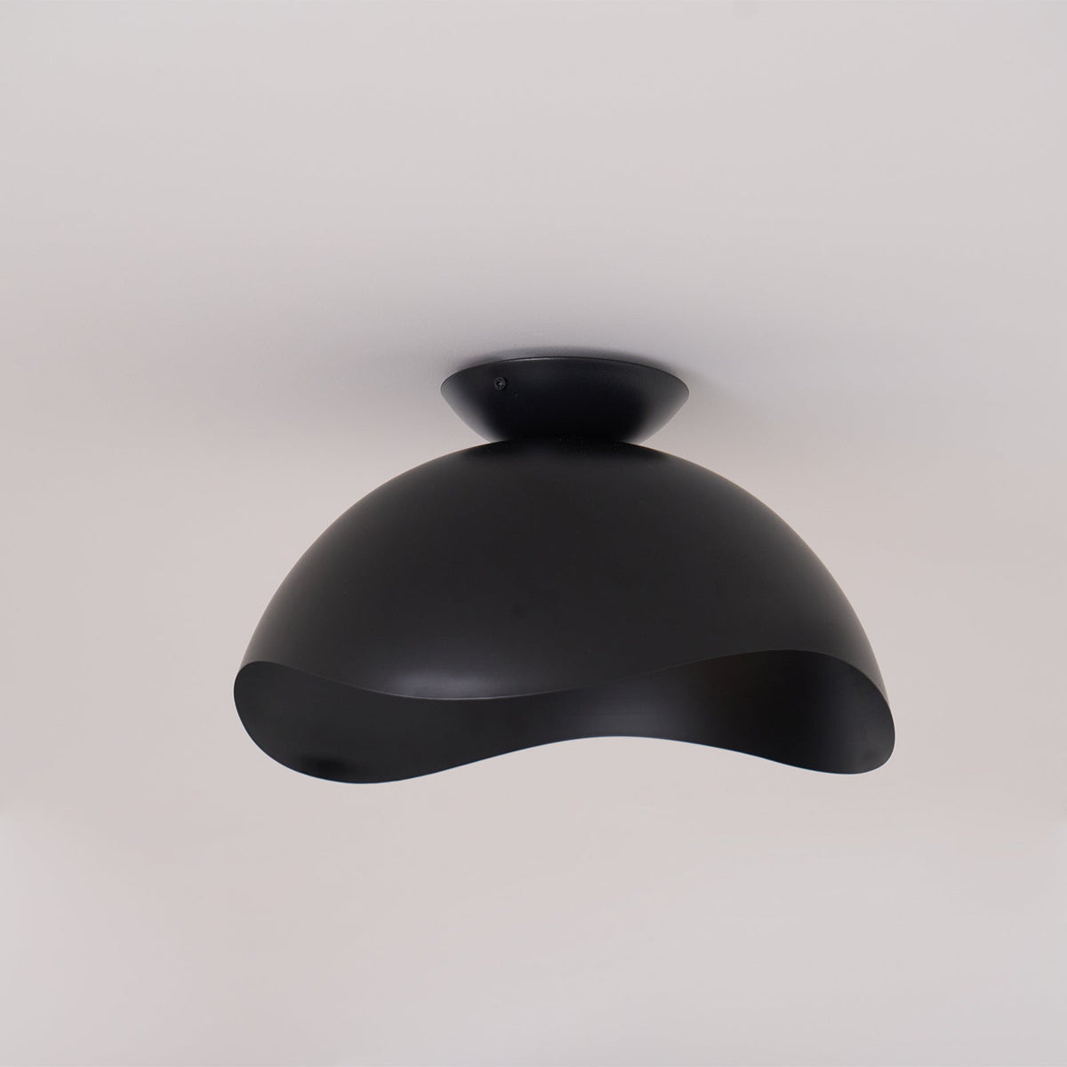 On a plain grey backdrop, this Clérachic ceiling light in black shows its full dome and wave-cut underside.
