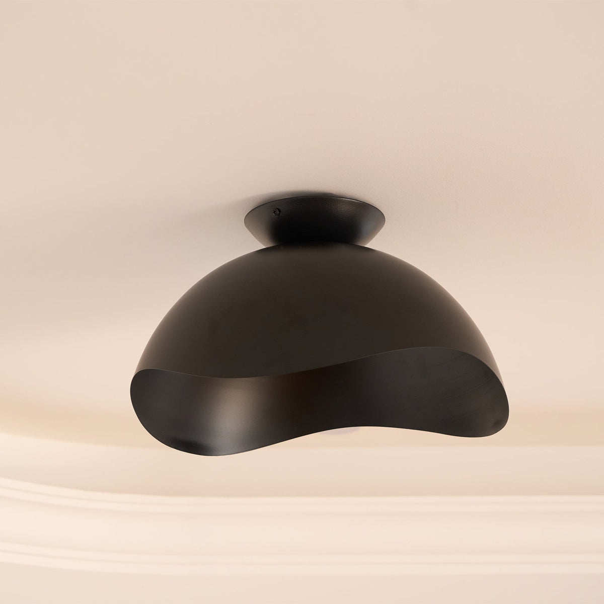 This Clérachic ceiling light in black sits close to decorative ceiling moulding on a soft pink-beige ceiling.