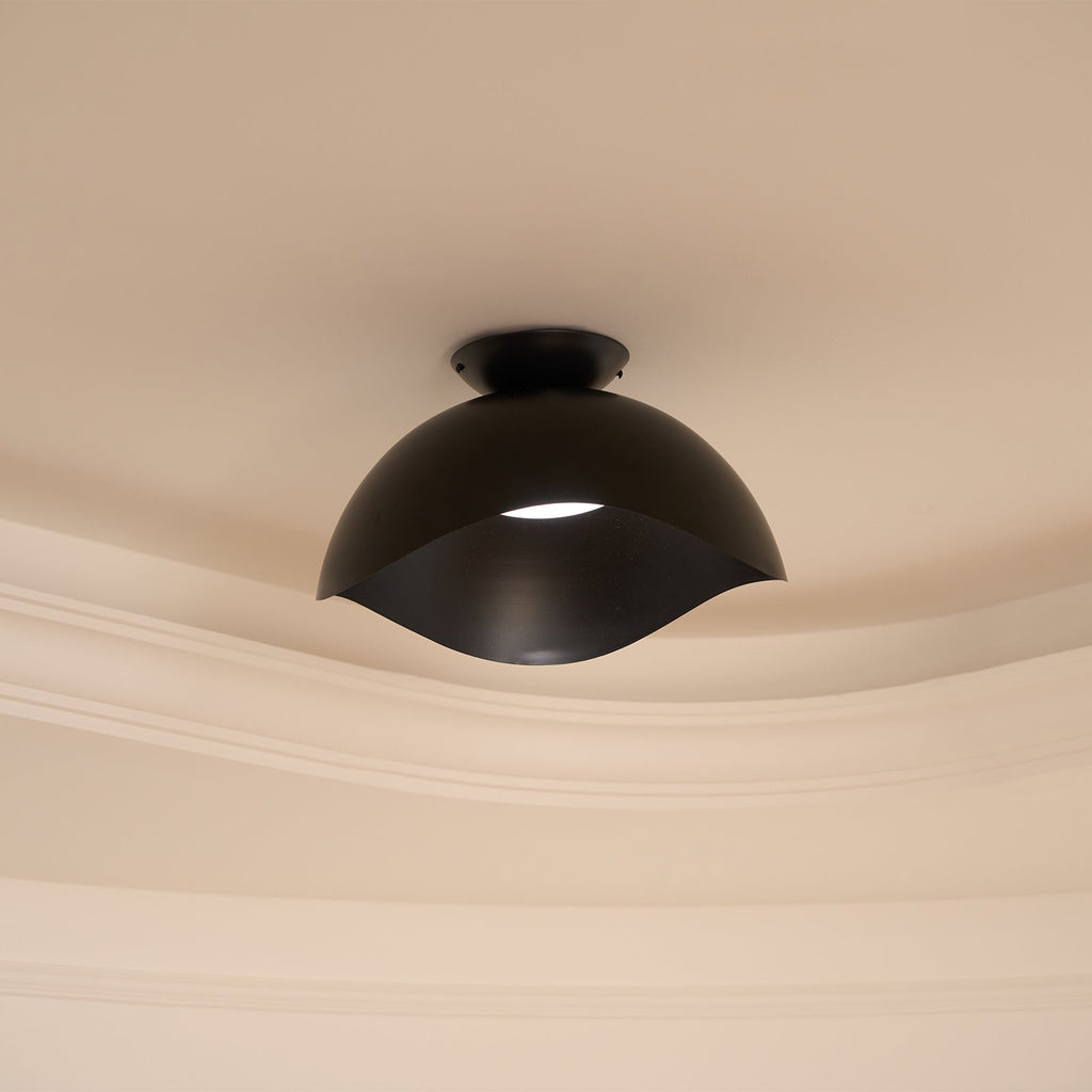 A sliver of light shows through the wave-cut gap of this Clérachic ceiling light in black, near ornate moulding.