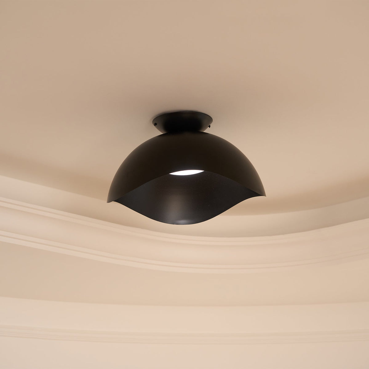 A sliver of light shows through the wave-cut gap of this Clérachic ceiling light in black, near ornate moulding.