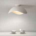 Sculptural white objects sit below this Clérachic ceiling light, which casts a soft glow across a plain grey wall.