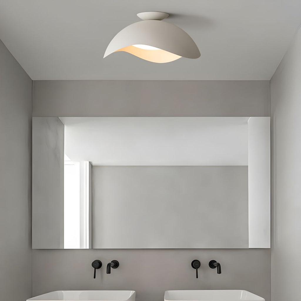 In a bathroom with a wide mirror and black fittings, the wave-shaped shade of this Clérachic light glows softly.