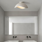 In a bathroom with a wide mirror and black fittings, the wave-shaped shade of this Clérachic light glows softly.
