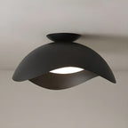 In black, this Clérachic ceiling light's wave shade glows warm underneath against a soft beige backdrop.
