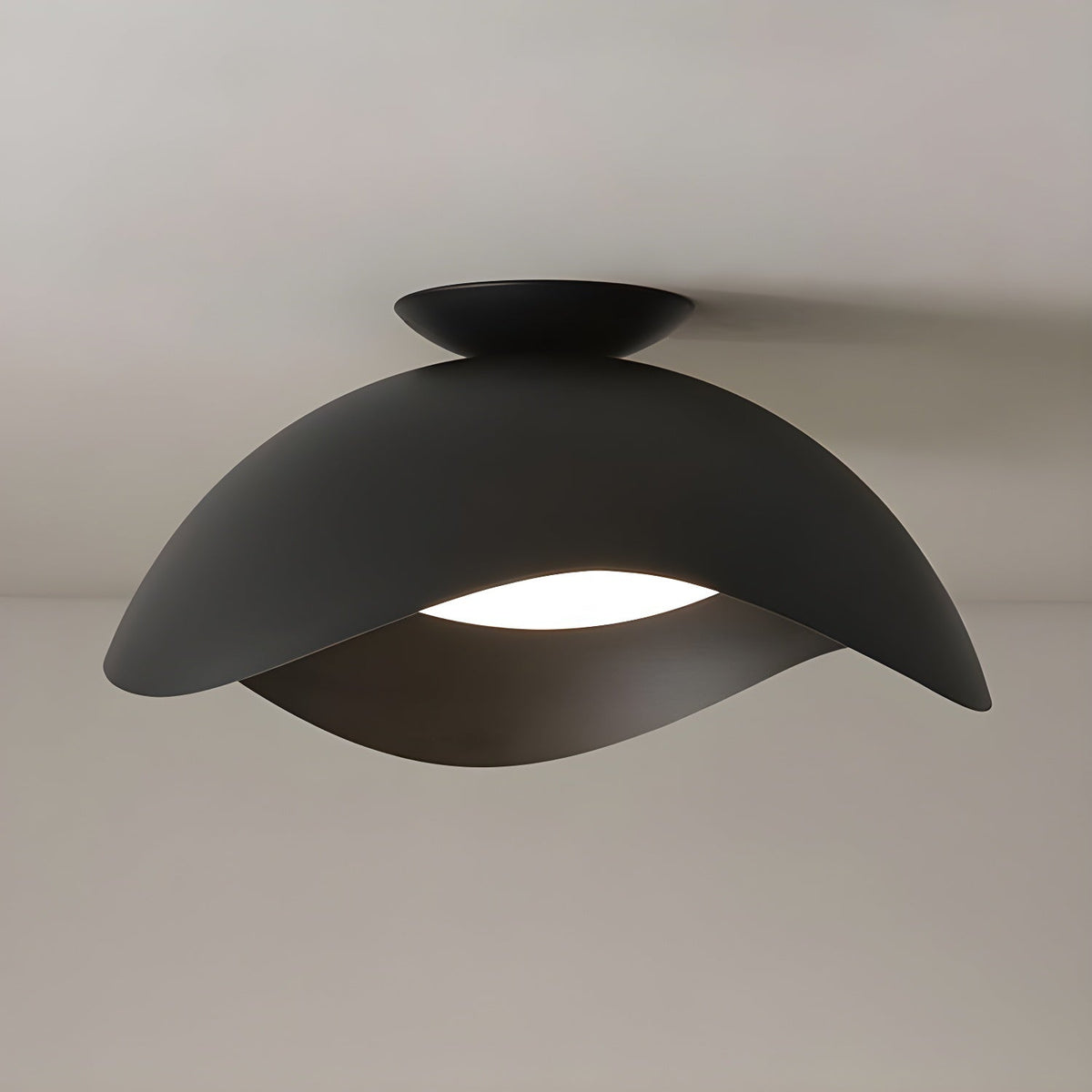 In black, this Clérachic ceiling light's wave shade glows warm underneath against a soft beige backdrop.