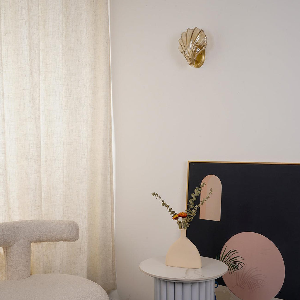 Above a round side table with a vase of eucalyptus and an arched print, this Clérachic wall light glows near sheer curtains.
