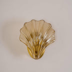 The amber glass shell of this Clérachic wall light glows softly against a plain off-white wall.