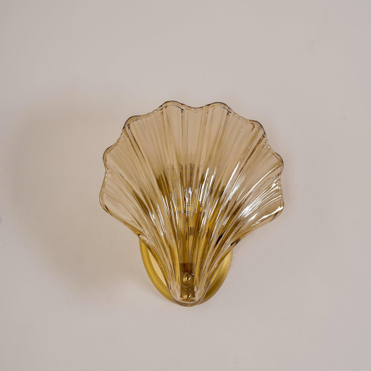 The amber glass shell of this Clérachic wall light glows softly against a plain off-white wall.