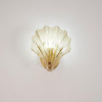 The ribbed glass shell of this Clérachic wall light glows softly against a plain wall, its brass plate visible below.