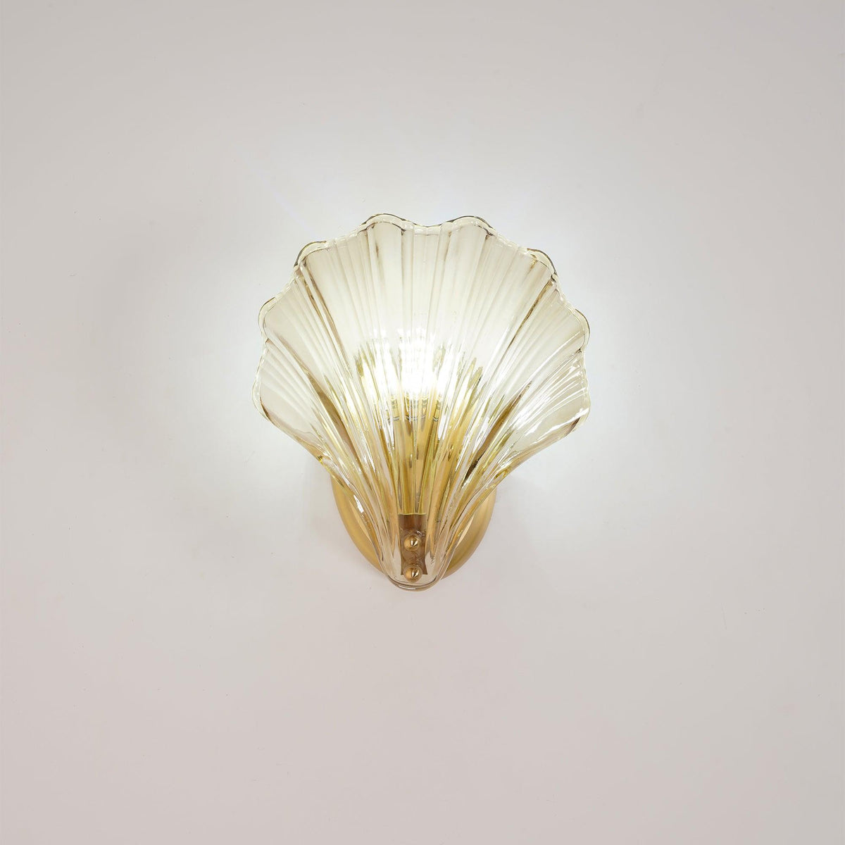 The ribbed glass shell of this Clérachic wall light glows softly against a plain wall, its brass plate visible below.