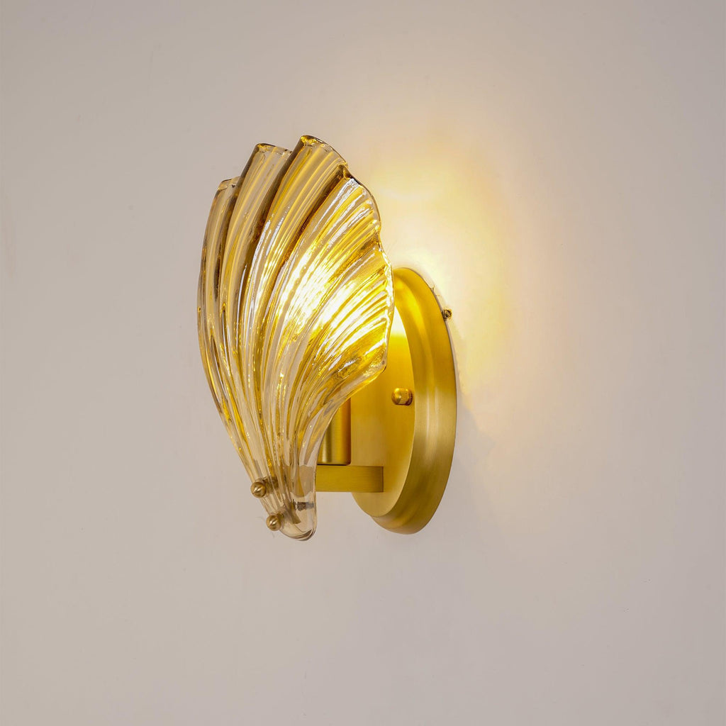 A side view shows the ribbed amber glass shell and brass wall arm of this Clérachic wall light, lit.