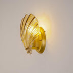 A side view shows the ribbed amber glass shell and brass wall arm of this Clérachic wall light, lit.