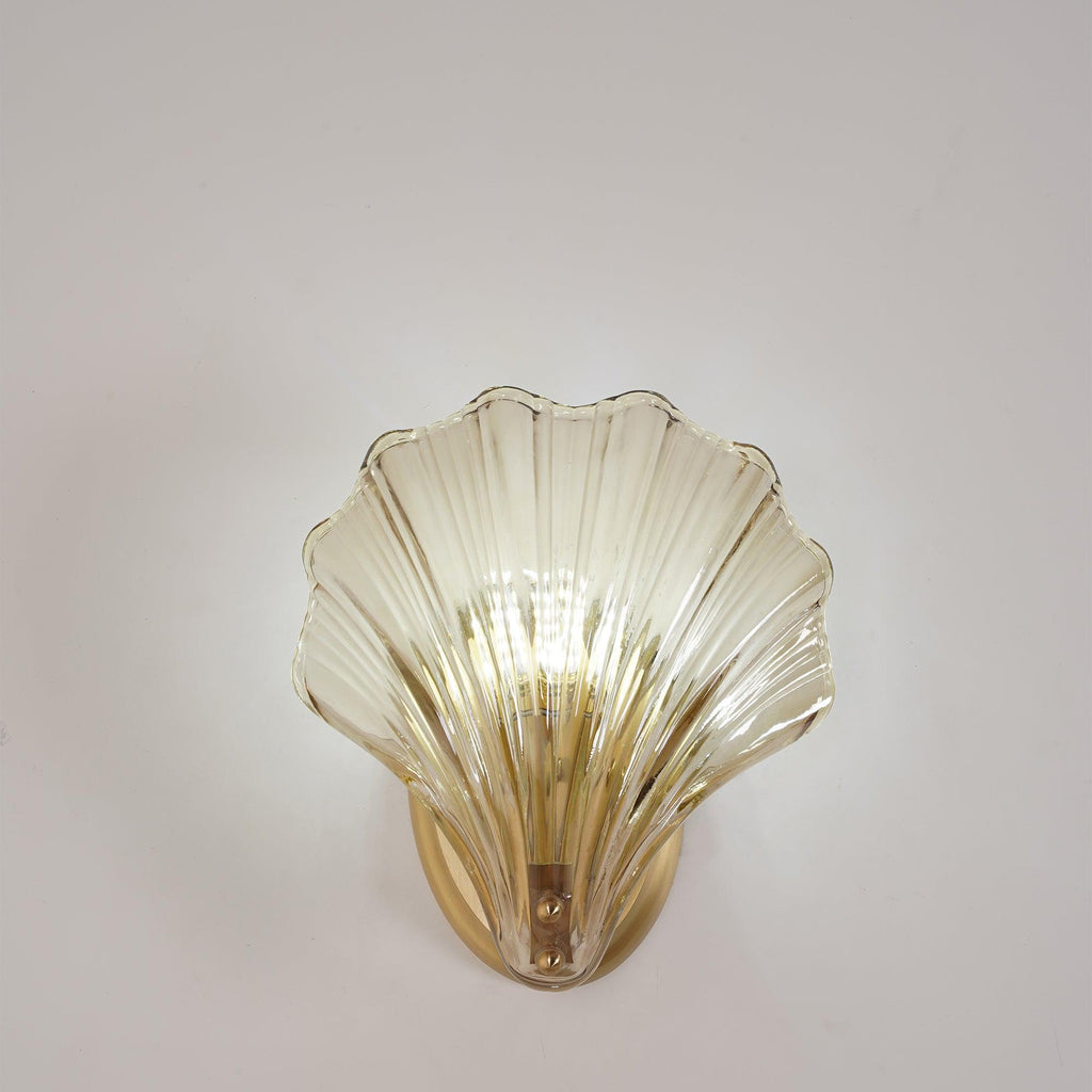The pale glass shell of this Clérachic wall light glows against a plain grey-white wall, photographed straight on.