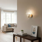 In a living room with a blue-cushioned sofa and a console table of books, this Clérachic wall light glows on a pale wall.