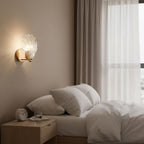Mounted between sheer-curtained windows, this Clérachic wall light glows softly above a bedside table with an alarm clock.