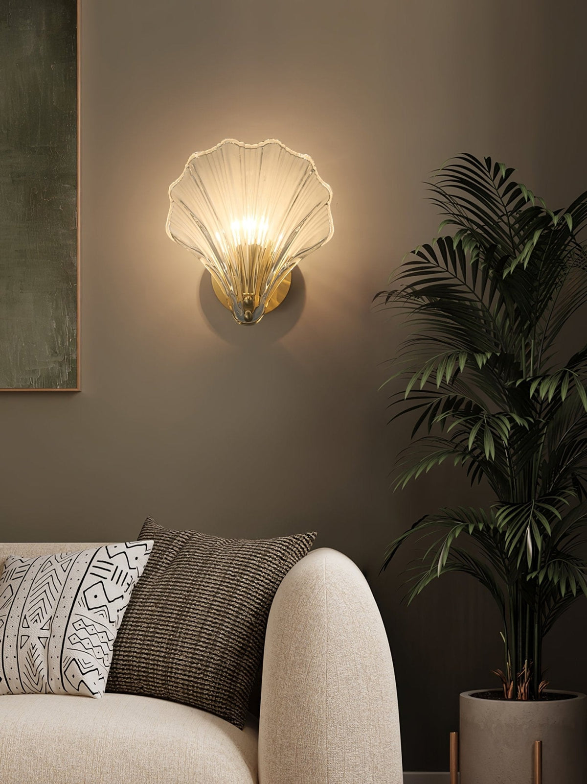 Framed by a potted palm and patterned cushions, this Clérachic wall light glows on a dark olive wall.