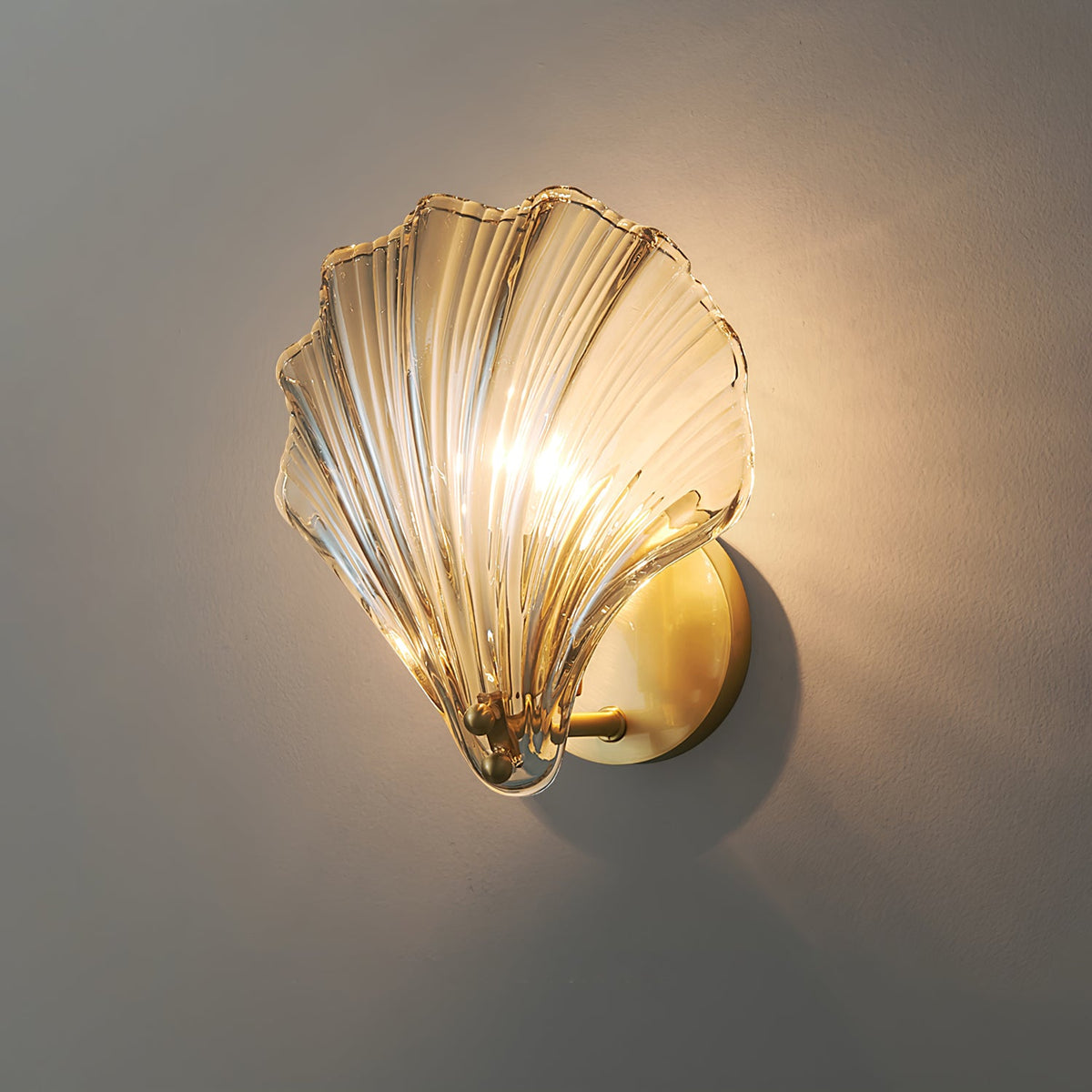 Seen from the same side angle, the amber glass shell of this Clérachic wall light glows against a grey wall.