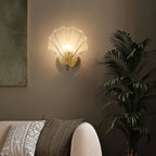 This Clérachic wall light glows on an olive-green wall beside a potted palm and patterned cushions.