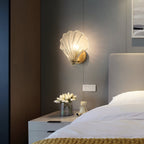 In a dark, moody bedroom, this Clérachic wall light glows amber above a nightstand set with white flowers.