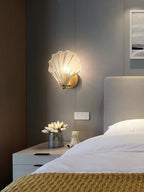 Mounted above a nightstand with tulip flowers, this Clérachic wall light glows beside an upholstered headboard.