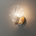 Seen from the side with a cast shadow, the clear glass shell of this Clérachic wall light glows on a grey wall.