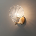 Seen from the side with a cast shadow, the clear glass shell of this Clérachic wall light glows on a grey wall.