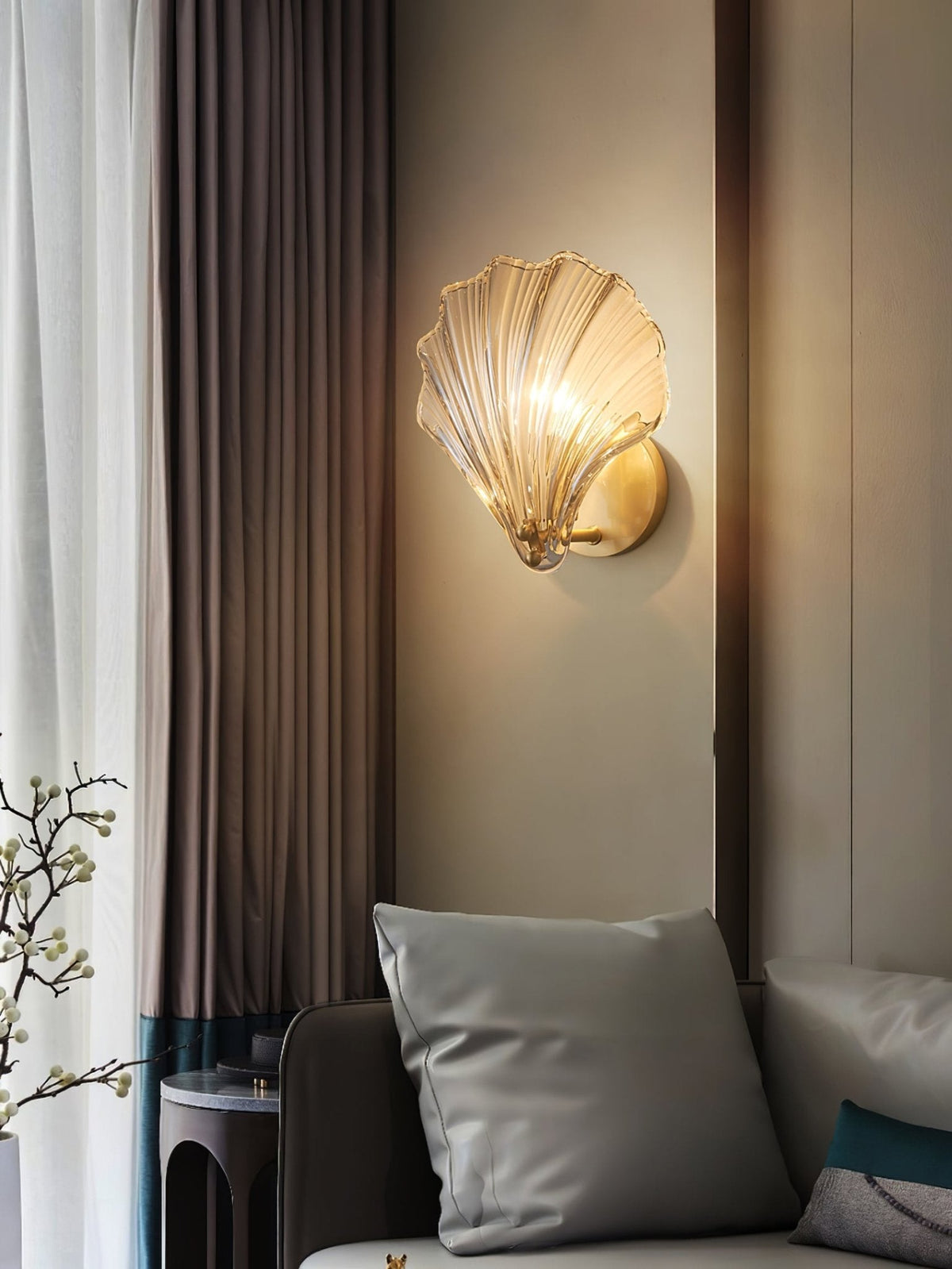 Beside a draped curtain and a flowering branch, this Clérachic wall light glows warmly in a moody reading nook.