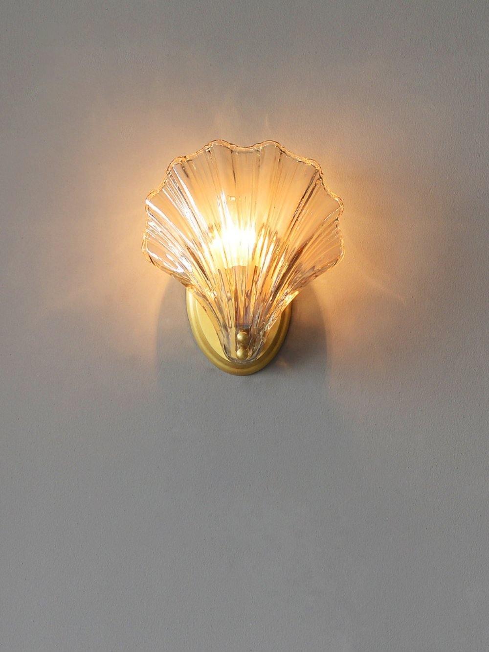 The amber glass shell of this Clérachic wall light glows warmly against a plain grey wall.