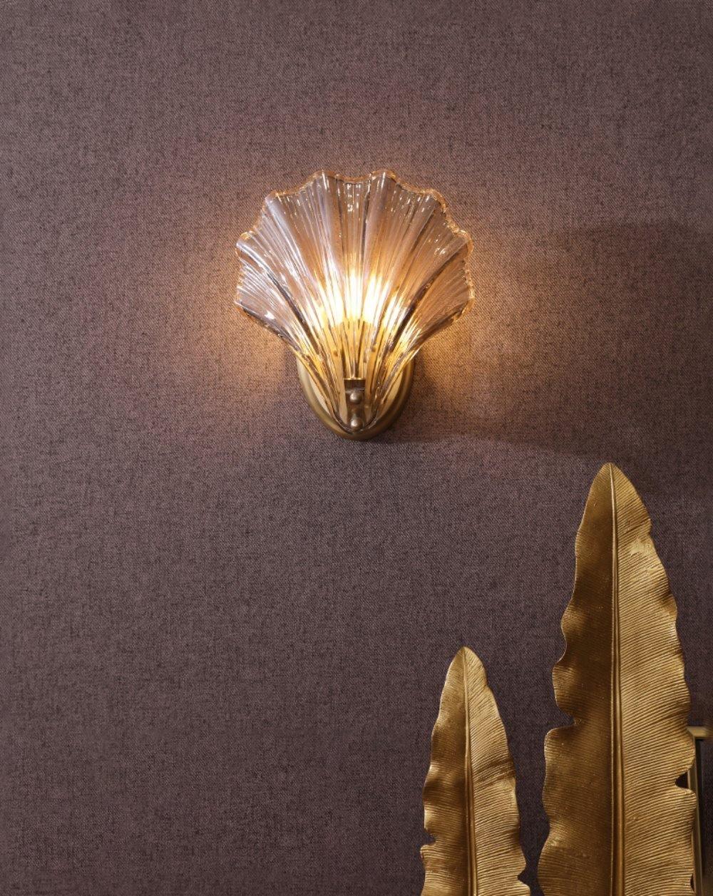 Against a plum textured wall with a gold leaf-shaped ornament nearby, this Clérachic wall light glows softly.