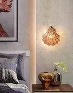 In a bedroom with plaster-textured walls, this Clérachic wall light glows beside a framed print and a small vase.