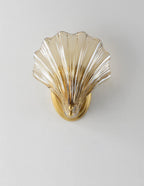 Photographed straight on, this Clérachic wall light's amber glass shell glows against a plain light grey wall.