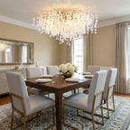 This Clérachic ceiling light, its gold branches strung with frosted glass discs, hangs above a walnut dining table set for six.