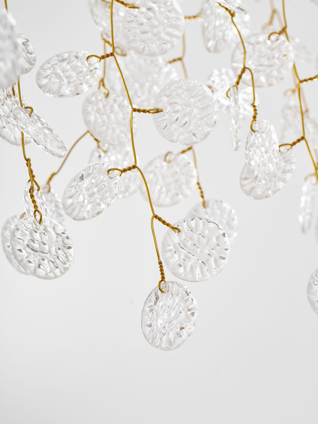 Close view of the textured clear glass discs threaded along the gold branches of this Clérachic ceiling light.