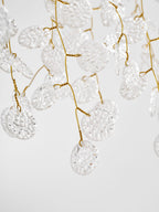 Close view of the textured clear glass discs threaded along the gold branches of this Clérachic ceiling light.