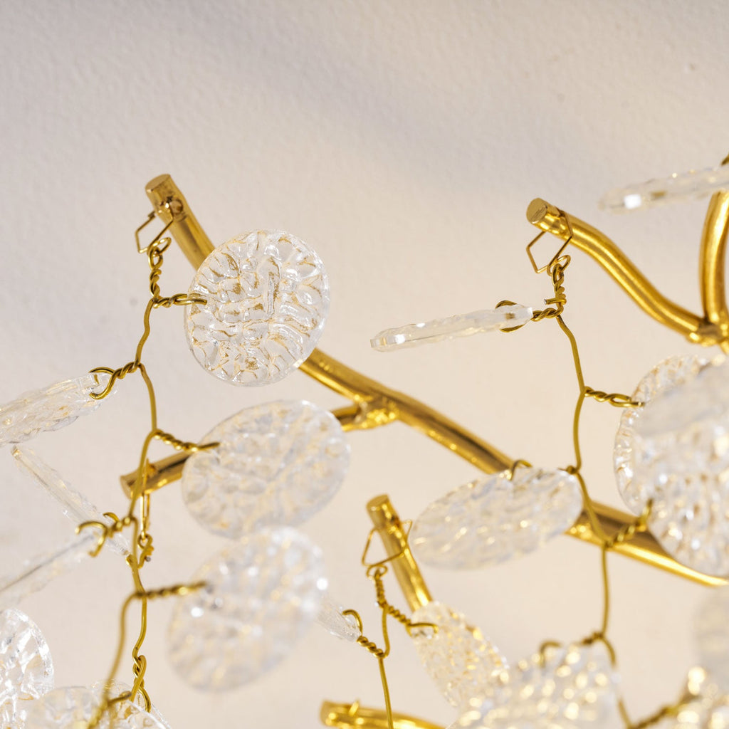 Extreme close view of the gold branches and clear glass discs on this Clérachic ceiling light, backlit in warm light.