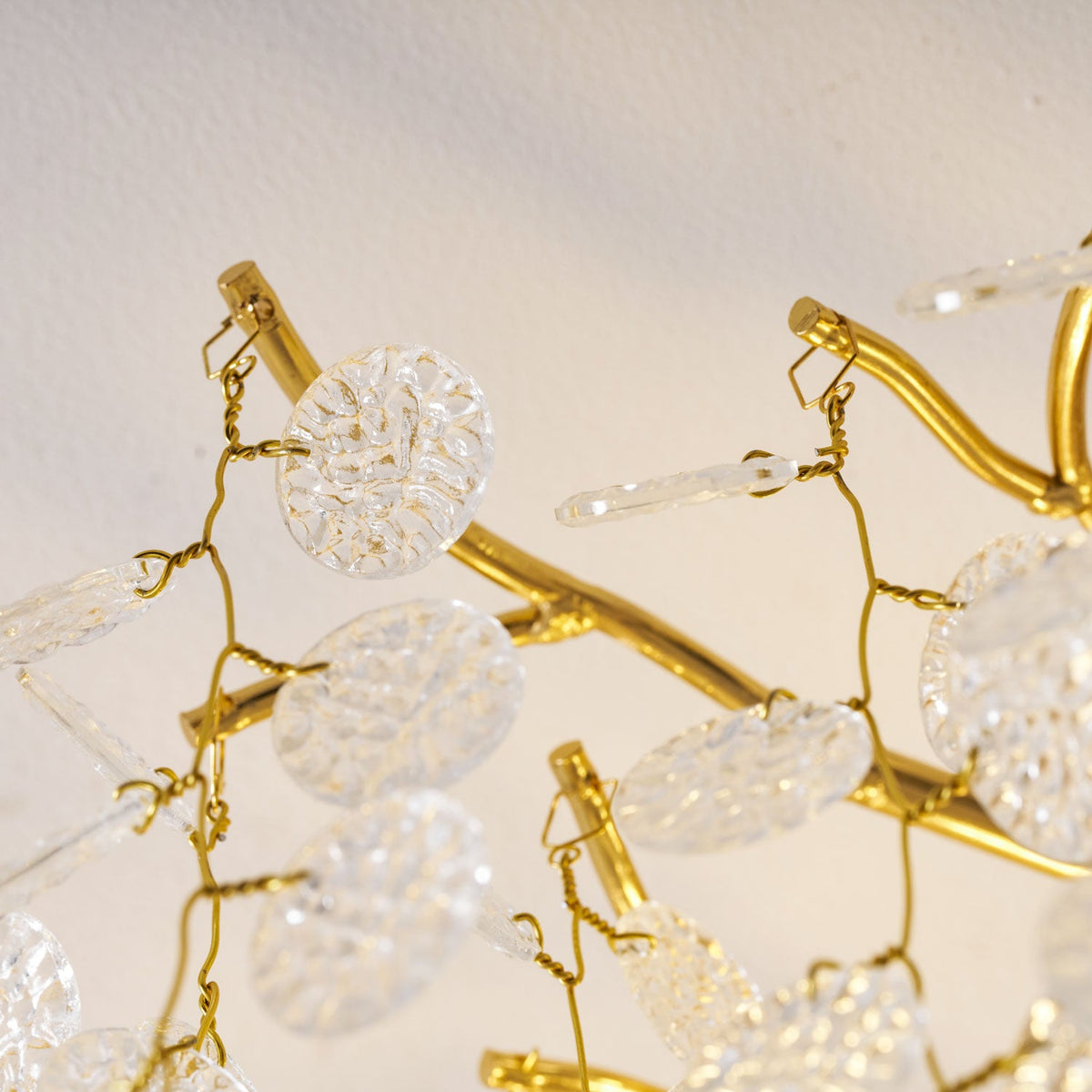 Extreme close view of the gold branches and clear glass discs on this Clérachic ceiling light, backlit in warm light.
