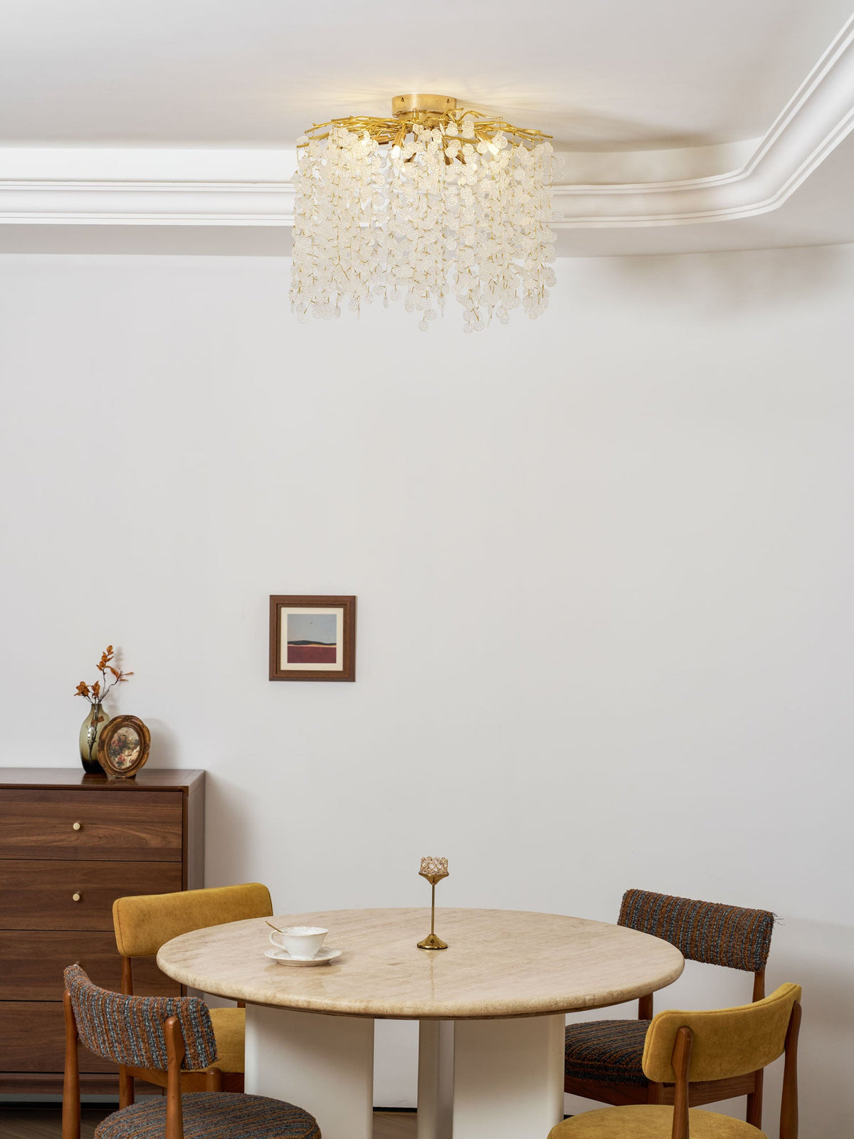 This Clérachic ceiling light hangs above a round marble dining table with mustard chairs, beside a dark wood sideboard and a framed print.