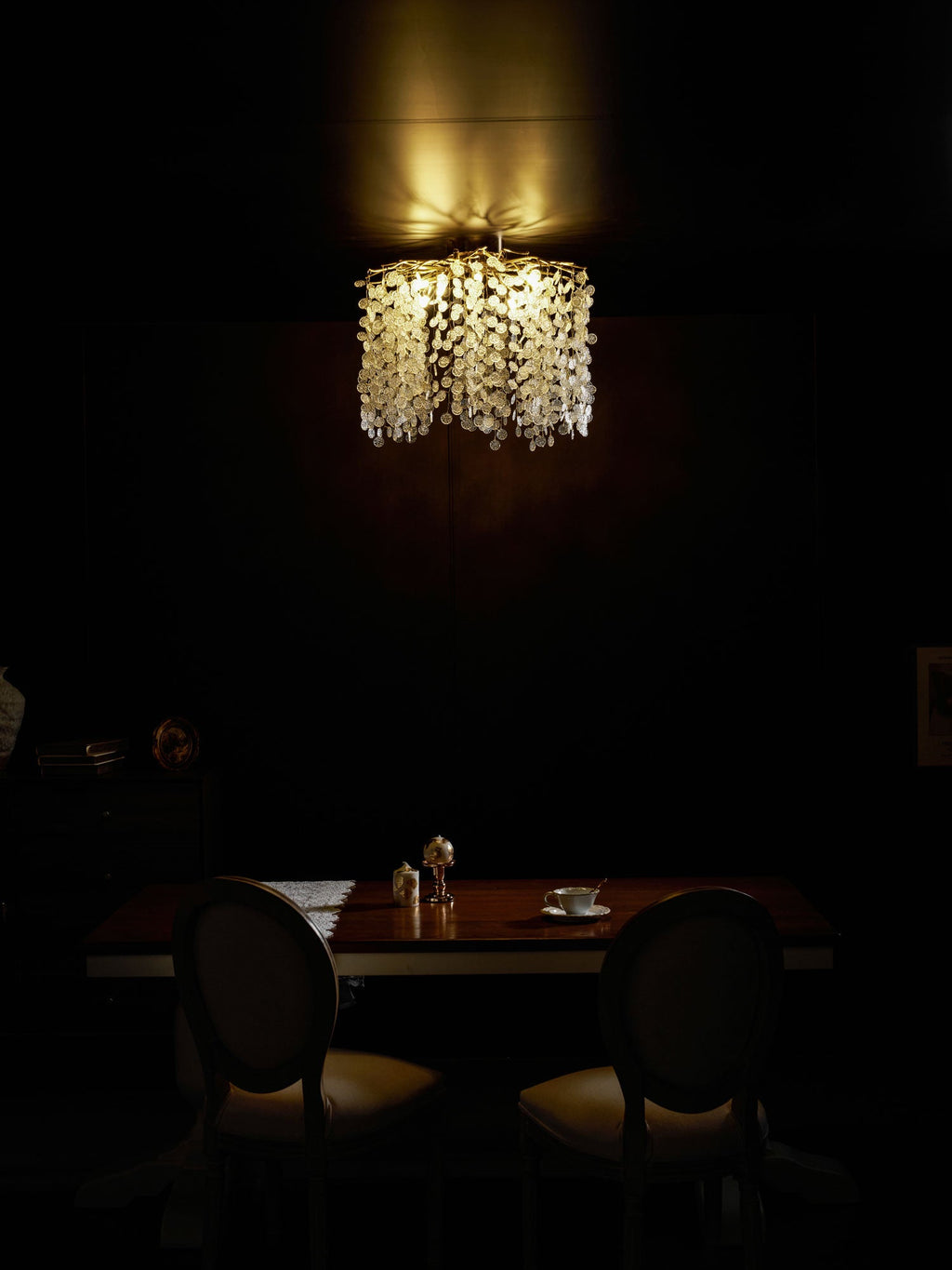 This Clérachic ceiling light glows warmly above a dark wood table set for two, in a dimly lit dining room.