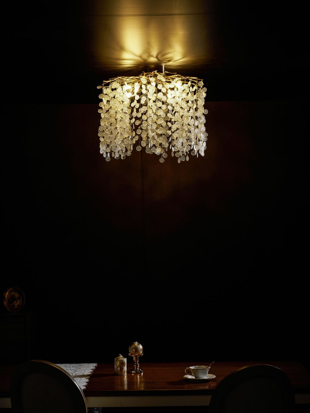 Seen from a different angle, this Clérachic ceiling light glows above a candlelit table in a dark, moody dining room.