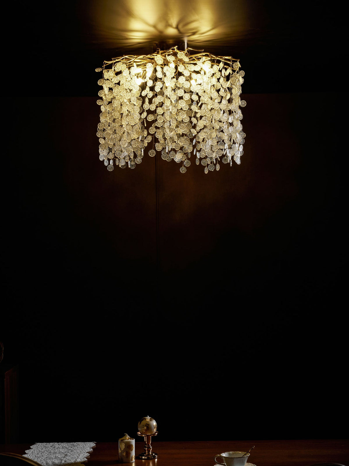 This Clérachic ceiling light glows above a table set with a small vase, in a dimly lit dark room.