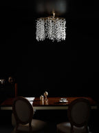 This Clérachic ceiling light in silver glows above a dining table with pedestal chairs, in a dark, moody room.