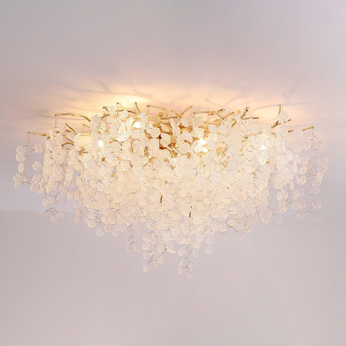 Lit against a plain grey backdrop, this Clérachic ceiling light's frosted glass discs glow warm above its gold branches.