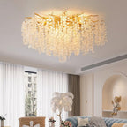 Lit above a living room seating area, this Clérachic ceiling light glows softly through frosted glass discs on gold branches, beside sheer curtains.