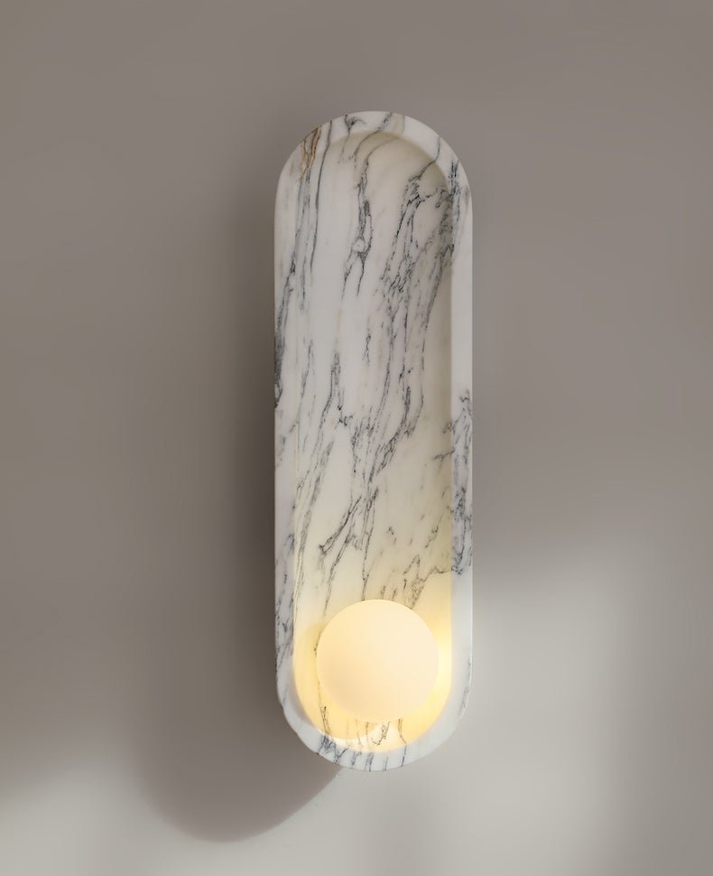 Warmly lit against a taupe wall, the Clérachic marble sconce casts a soft shadow from its glowing opal sphere.