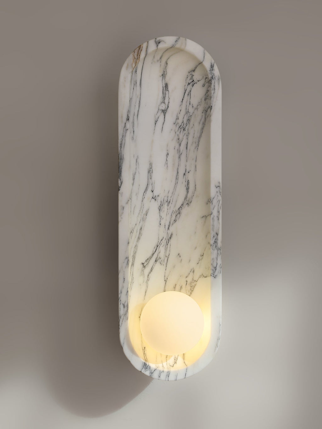 Seen at an angle on a grey-brown wall, the lit Clérachic sconce throws a soft shadow beside its marble form.