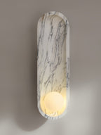 Seen at an angle on a grey-brown wall, the lit Clérachic sconce throws a soft shadow beside its marble form.