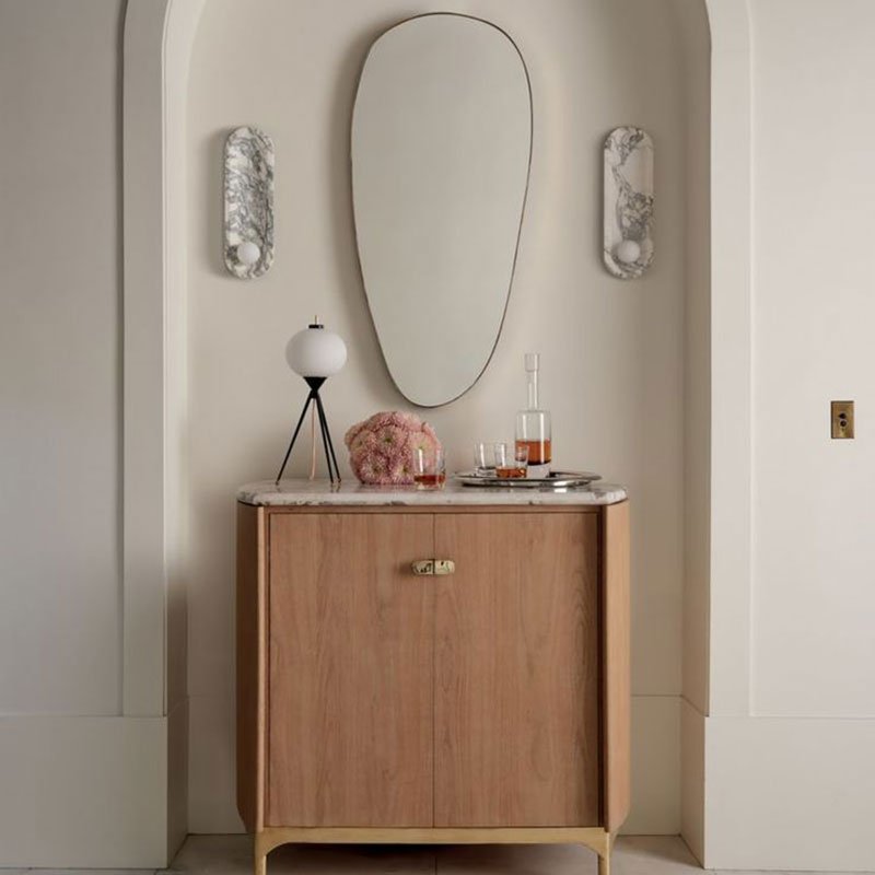 A pair of Clérachic wall lights flanks an oval mirror above a wooden console table in this entryway scene.