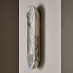 Another close angle on the Clérachic wall light's brass mounting edge, its marble form unlit against a beige wall.