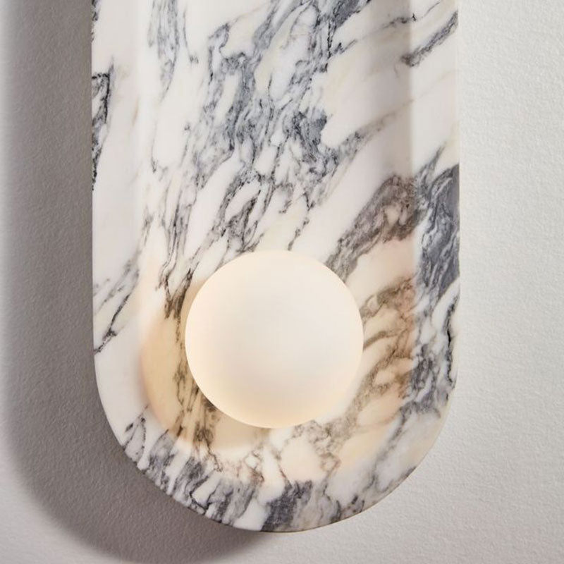 Viewed from above, the Clérachic sconce's opal sphere glows warm against the grey veining of its marble top.
