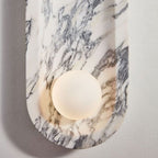 Viewed from above, the Clérachic sconce's opal sphere glows warm against the grey veining of its marble top.